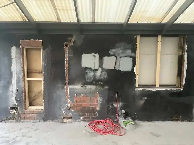 Before: patched and painted brick wall under a pergola, window and door openings framed
